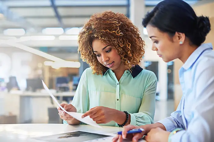 Two business women going over paperwork at a desk.