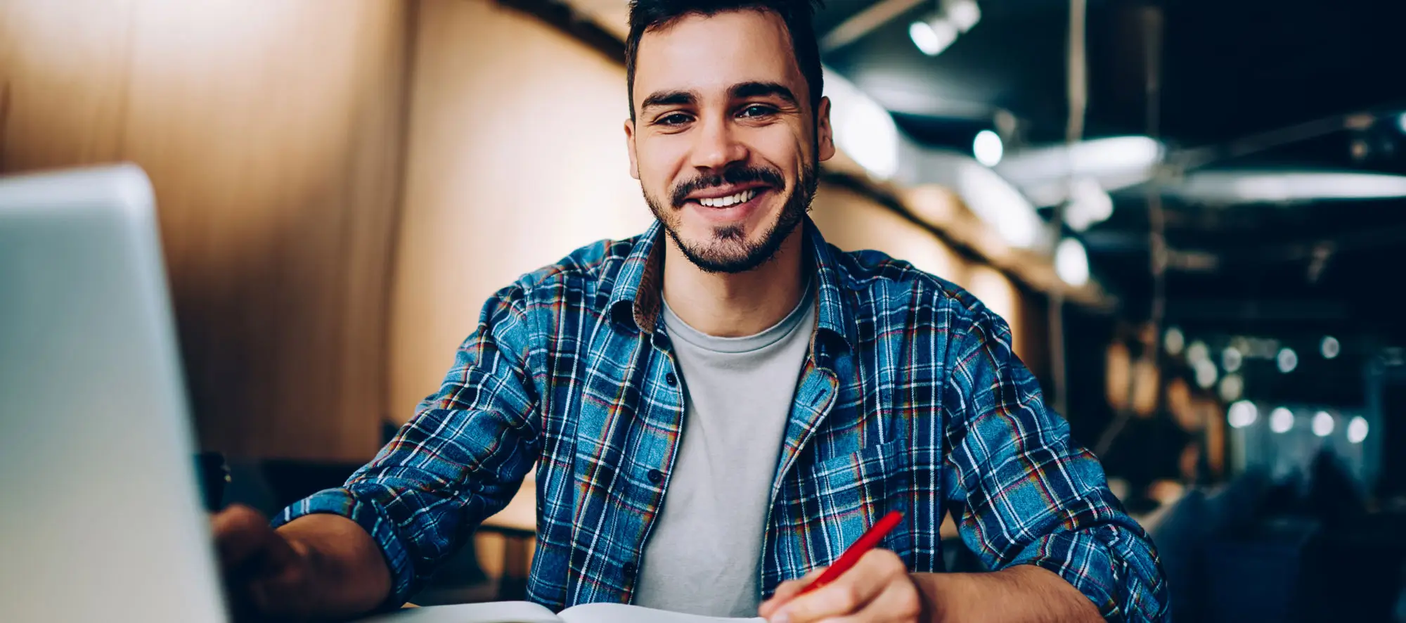 Cheerful male student enjoying learning in coworking office using laptop computer for research.