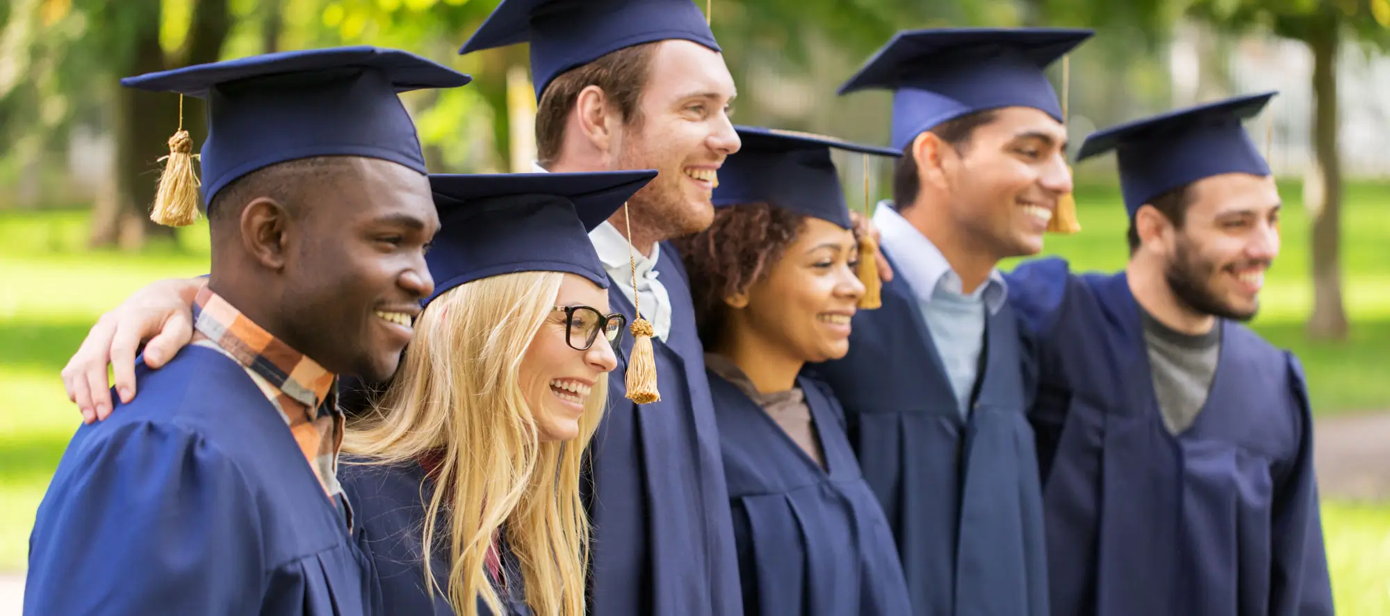 Graduation and people concept - group of happy international students in mortar boards and regalia gowns outdoors