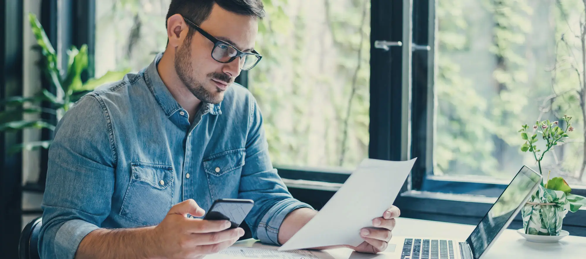 Small business owner in office looking at and working with laptop and income tax return papers.