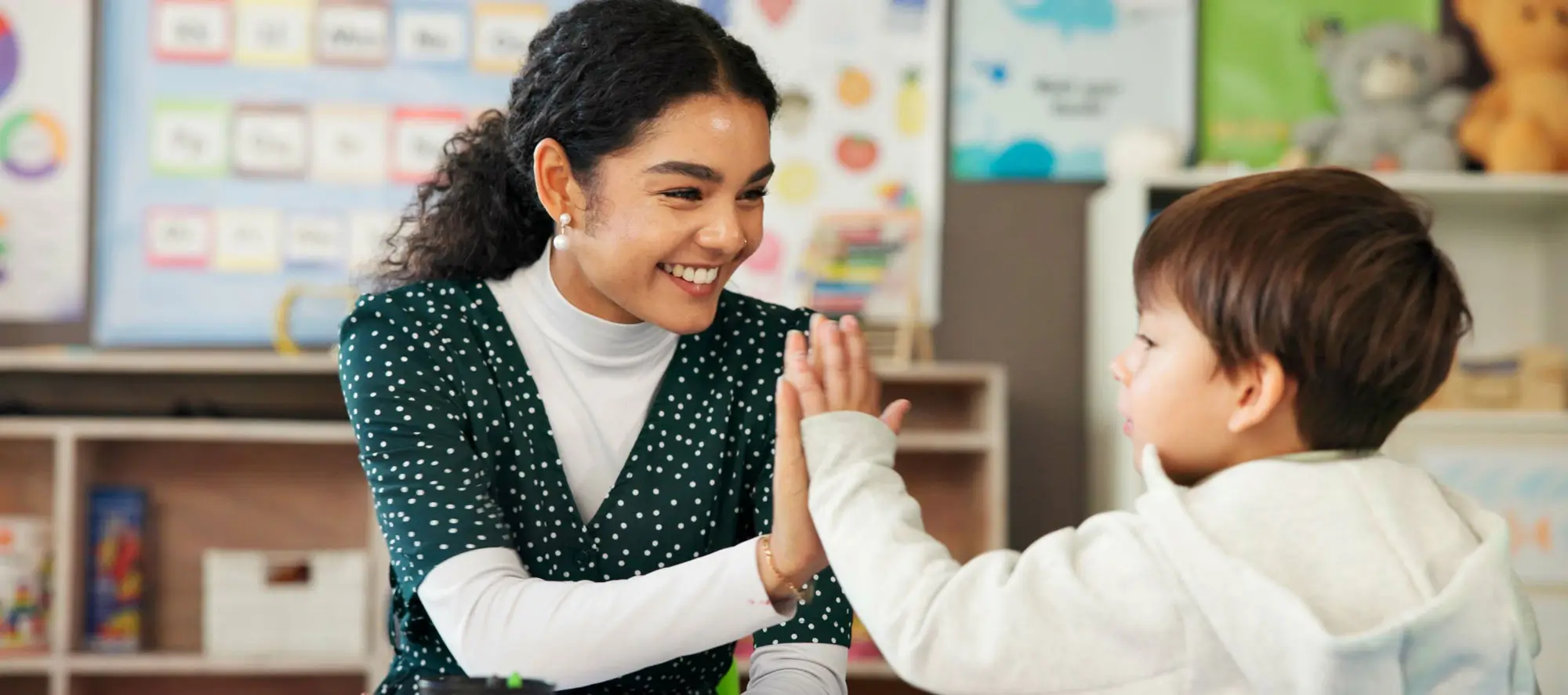 teacher and child with high five in classroom for learning support