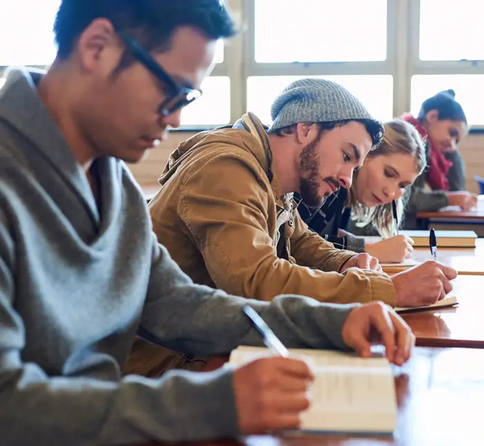 College students, writing on desk in classroom with books for english literature or language for exam.