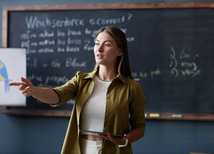 Female Teacher with Table Speaking to Student in English Class at Language School