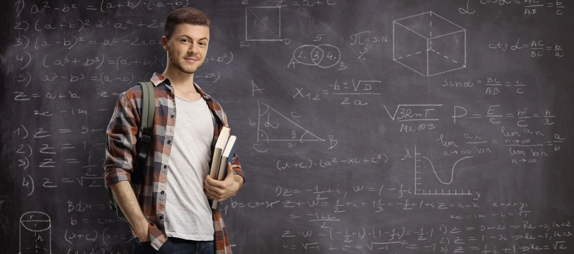 Male student posing in front of a blackboard written with math formulas and equations 