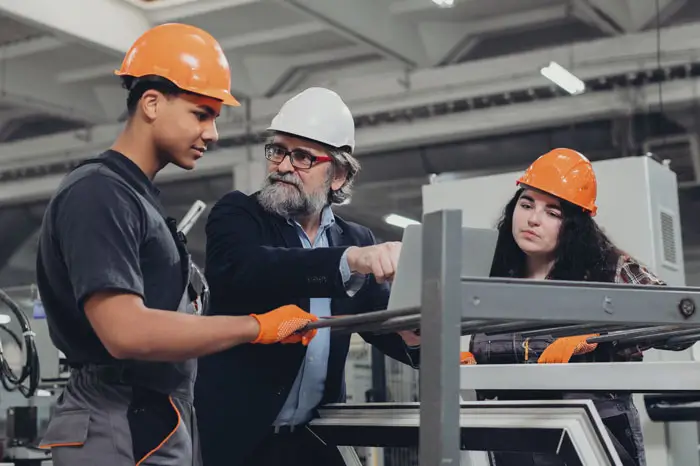 Experienced engineer guiding young manufacturing apprentices in factory.