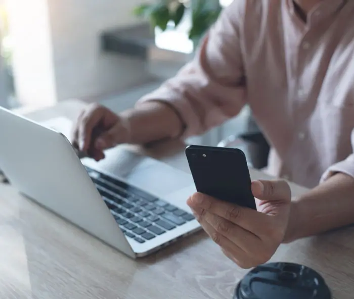 Close up of casual business man working on laptop computer, browsing internet and using mobile smart phone