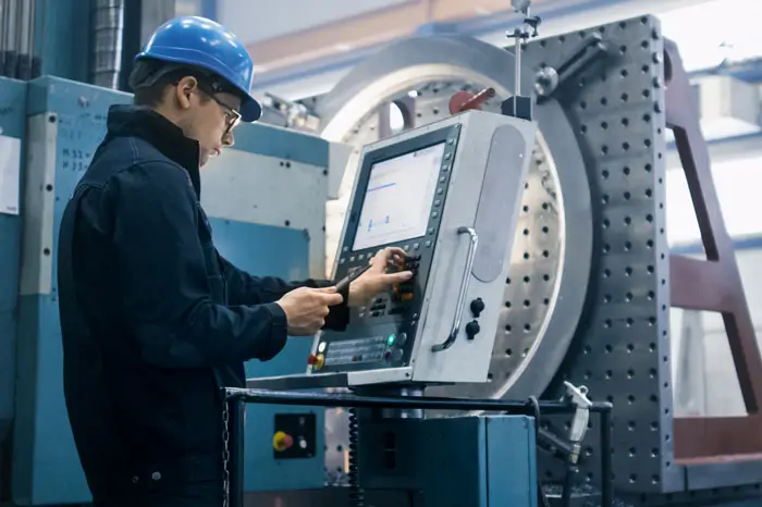 Factory worker is programming a CNC milling machine with a tablet computer.