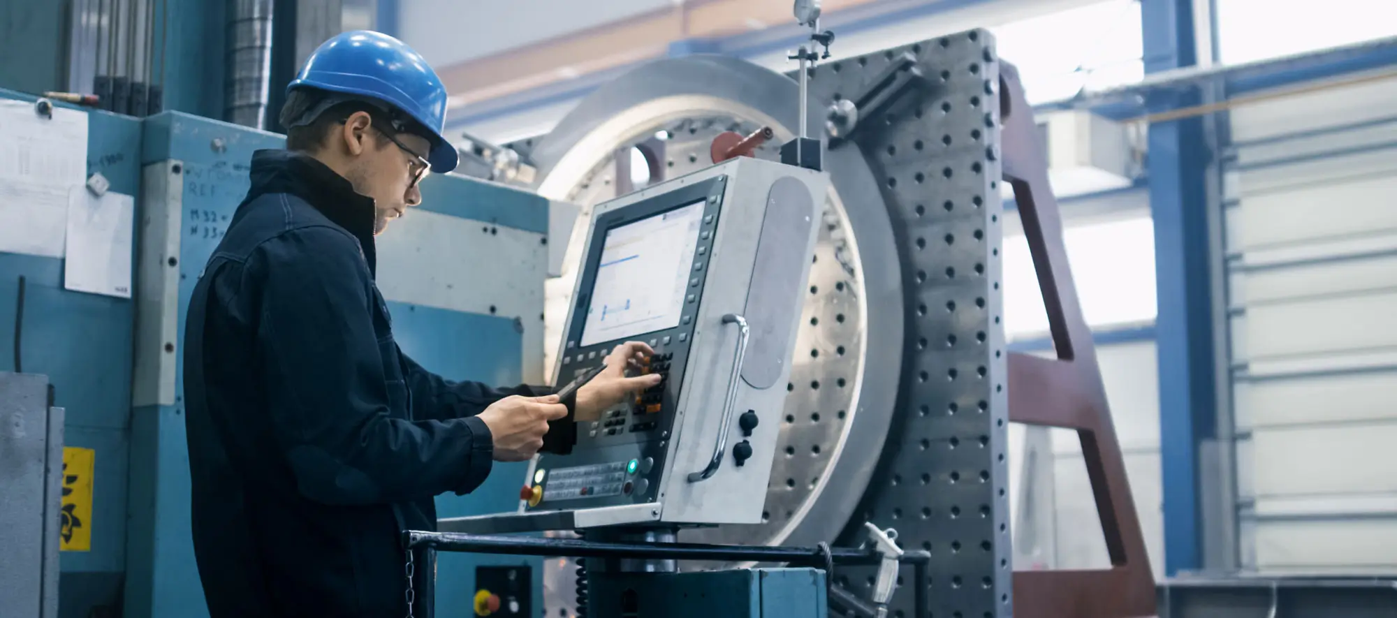 Factory worker is programming a CNC milling machine with a tablet computer.