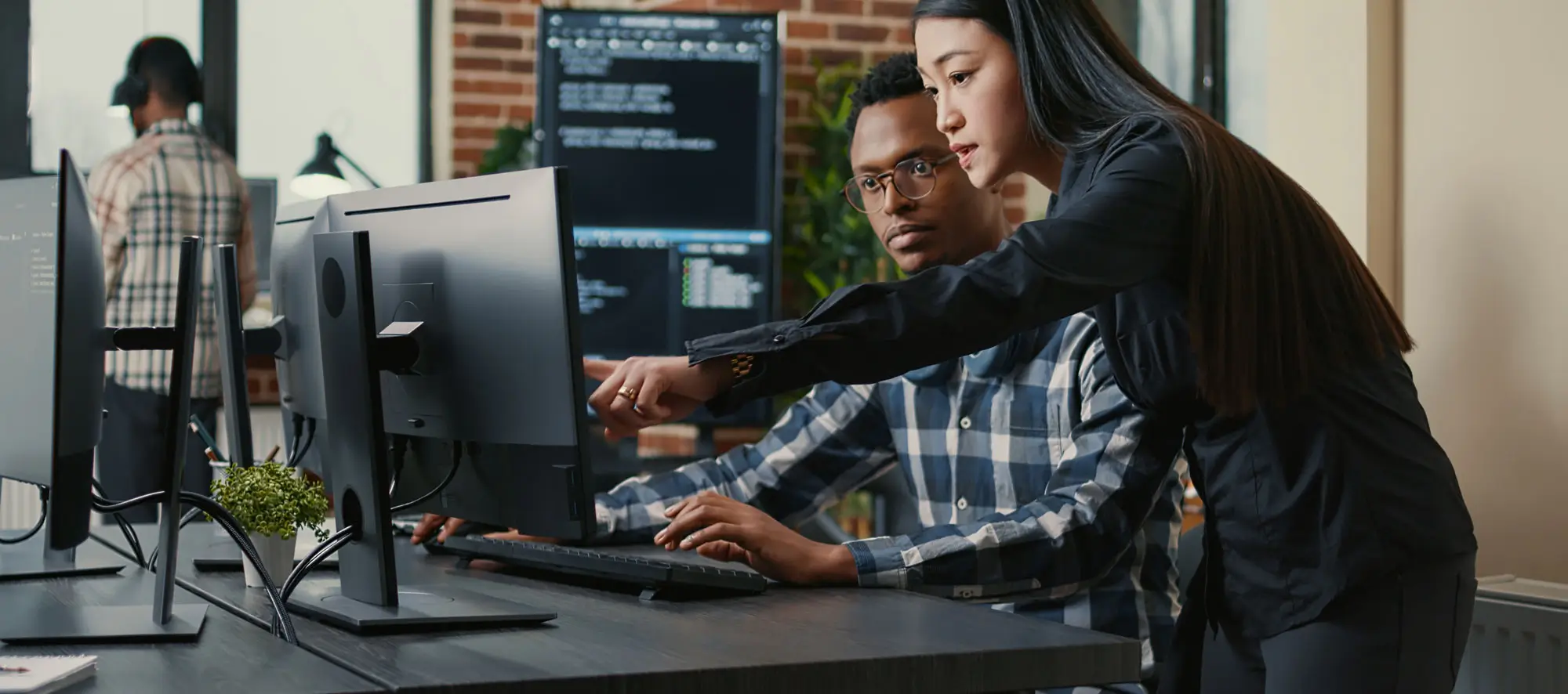 Two programers holding laptop with coding interface walking towards desk and sitting down