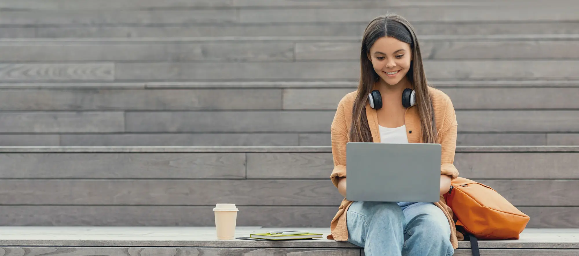 Cheerful young woman in stylish casual outfit university student using laptop computer outdoors.