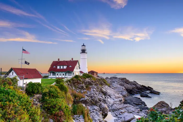 Scenic view of a white lighthouse overlooking a rocky cliff and a sea at sunset