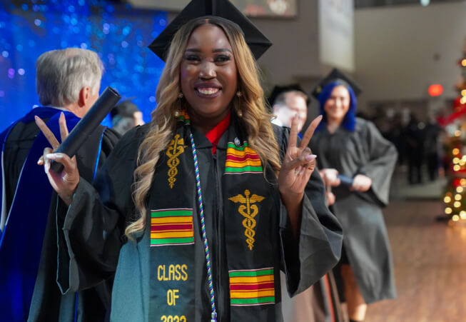 Graduating student walking across stage showing peace signs with her hands holding her diploma.