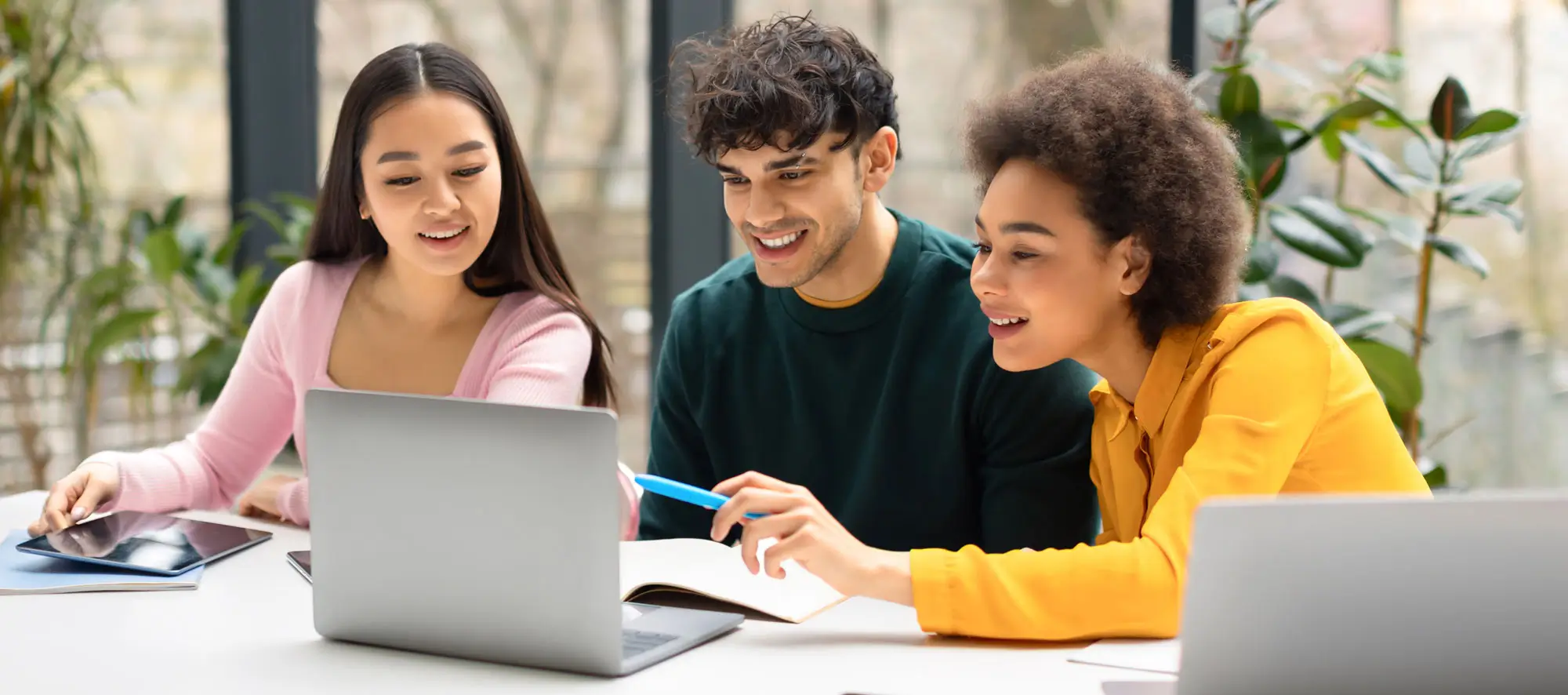 Happy students sitting at desk in coworking space and using laptop.