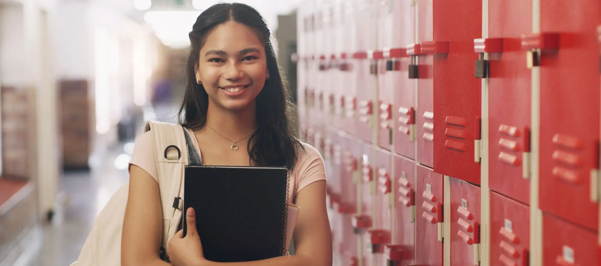 Female student holding books standing next to red lockers