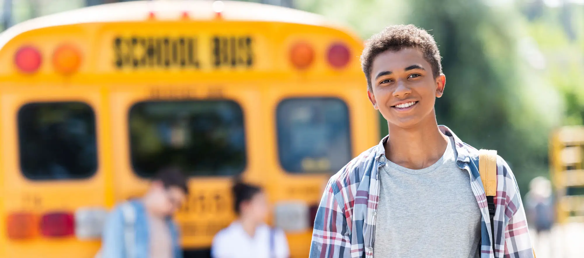 Happy teen african american schoolboy looking at camera in front of school bus
