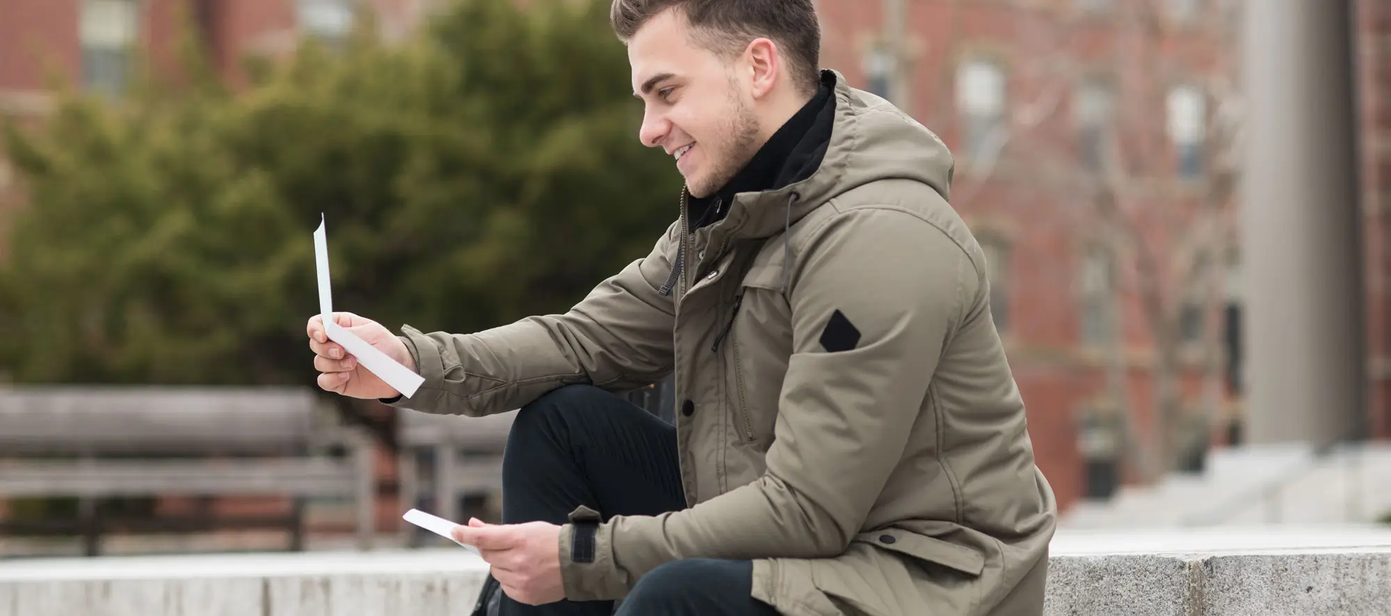 Happy student man reads refund letter sitting in campus.
