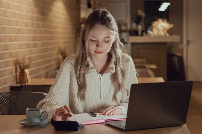 Female student with laptop and calculator running numbers.