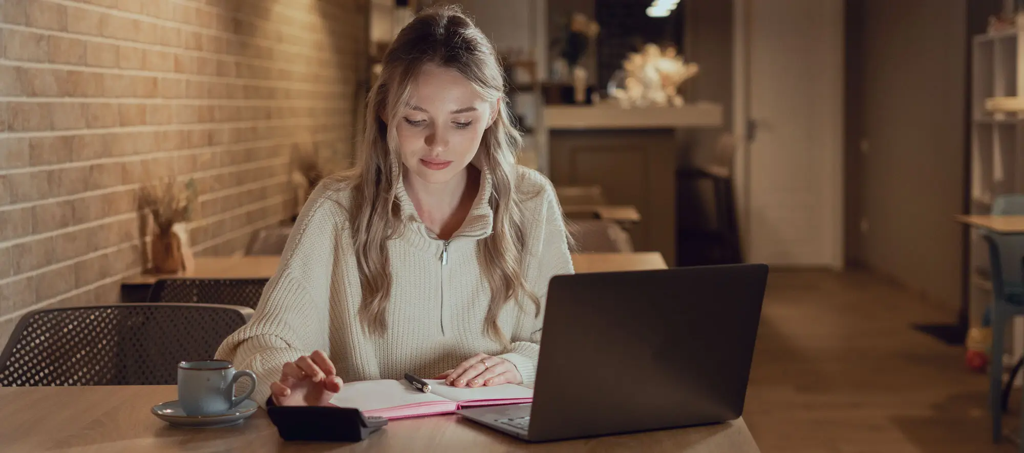 Female student calculates monthly expenses using calculator and laptop.