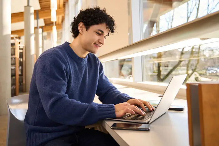 Young male student using a computer in college library.