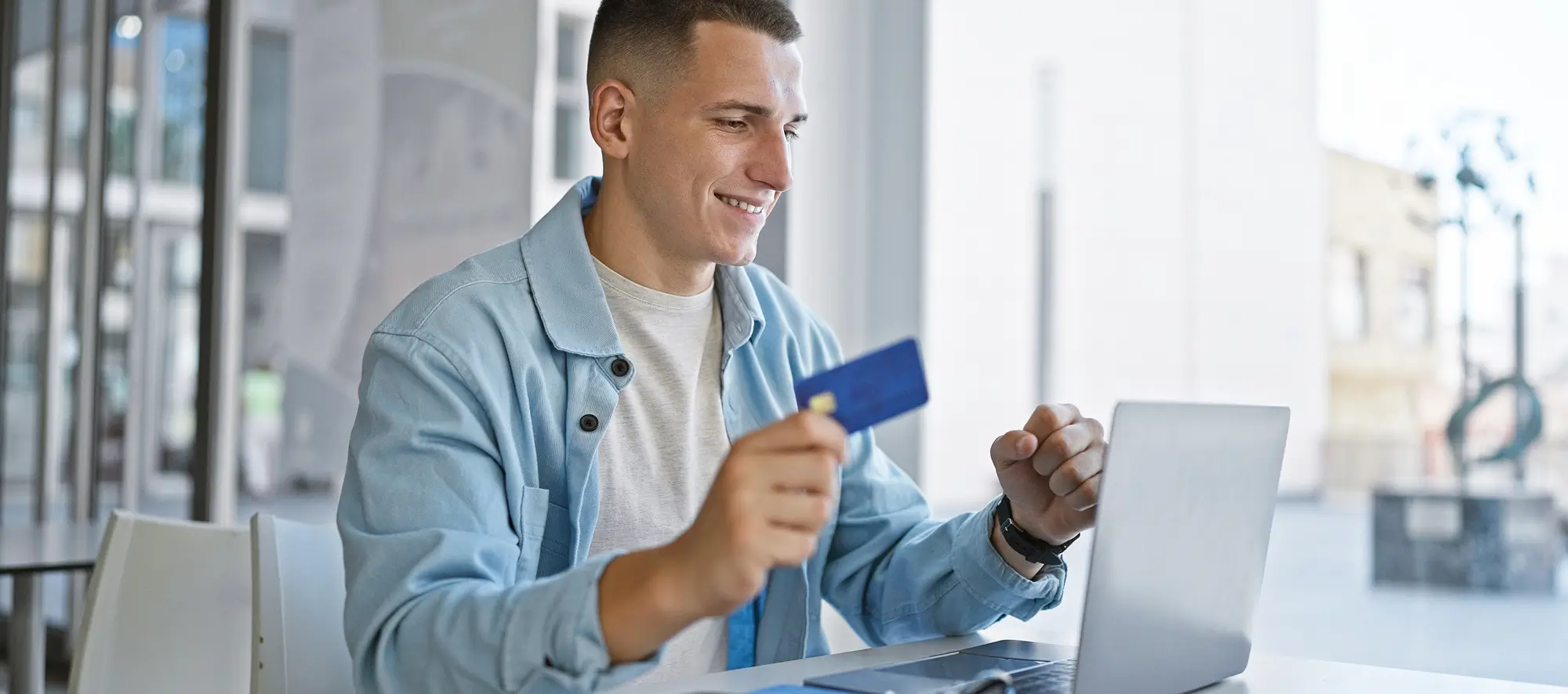 Smiling young man with credit card using laptop at college campus library.