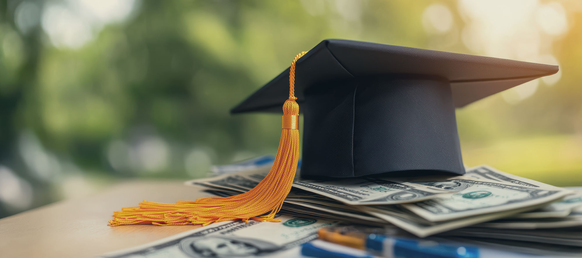 Graduation cap on stack of cash: symbol of education costs and financial planning.