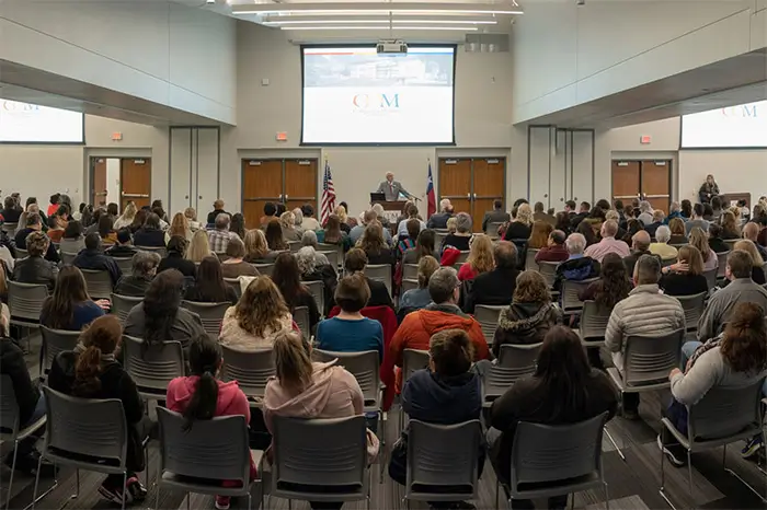 COM conference center filled with people viewing a presentation on projector screen