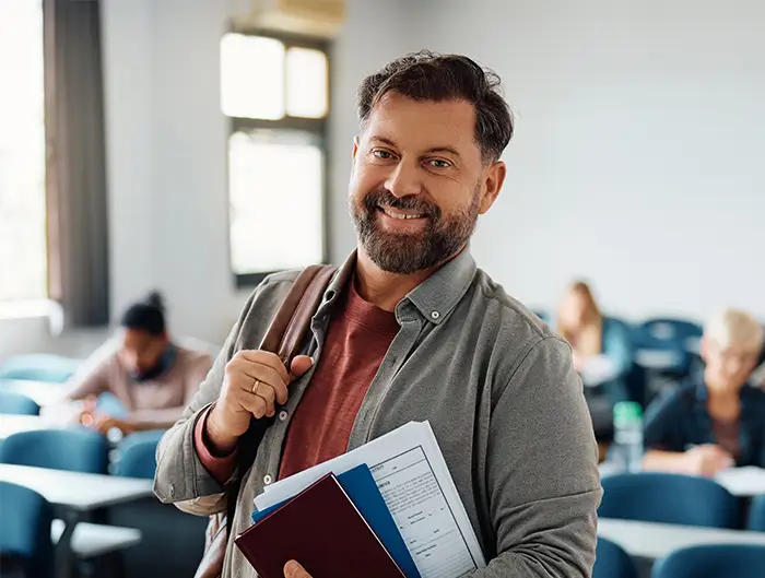 Thirty year old man in a classroom holding books. 