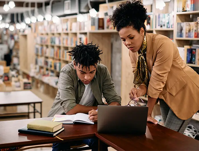 student at computer getting help from tutor.