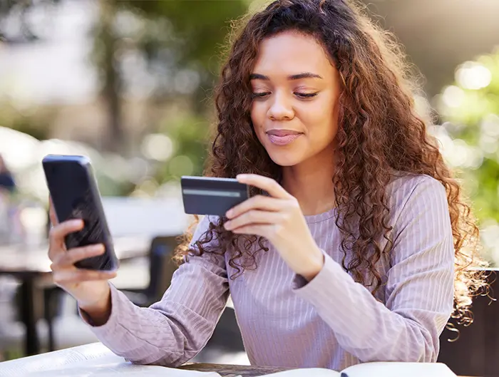 Student looking at phone with credit card in hand.