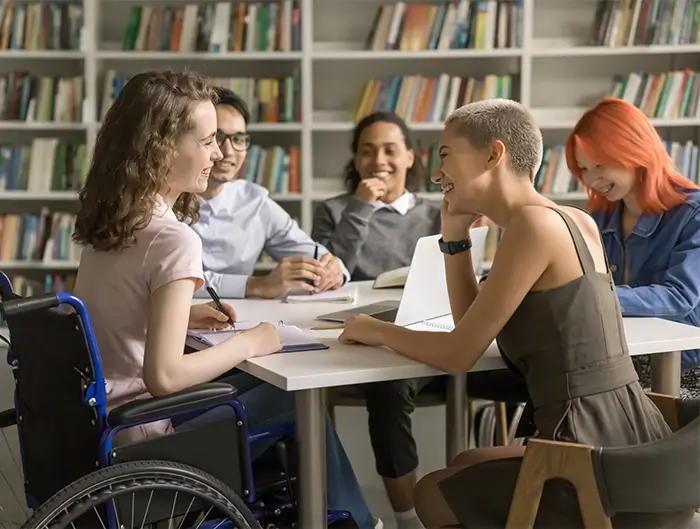 Diverse ground of students talking at a table in the library.