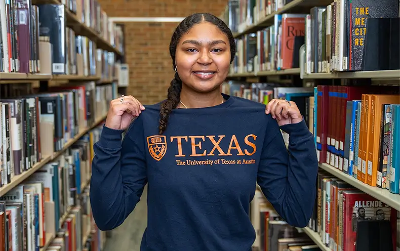 COM Collegiate High School Student Grace Pope Wears a University of Texas at Austin Shirt in the COM Library.