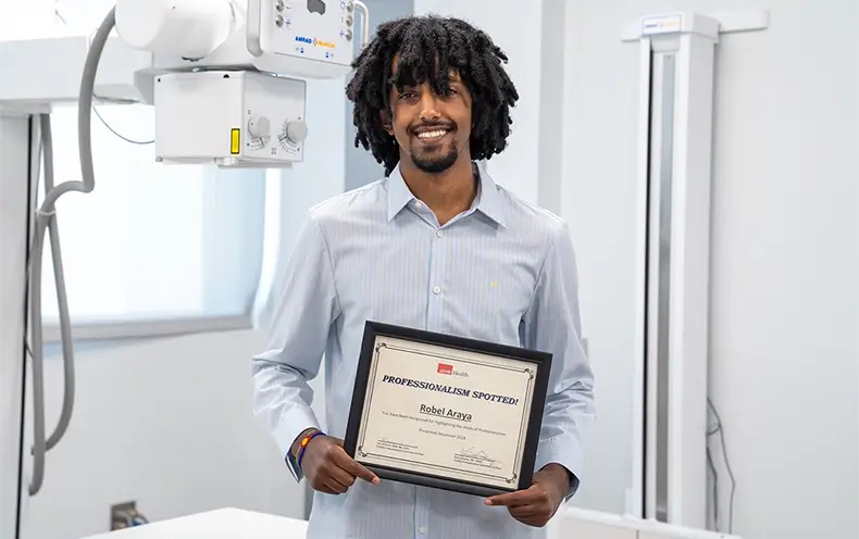 Robel Araya stands with his professionalism award in the College of the Mainland radiologic technology classroom.