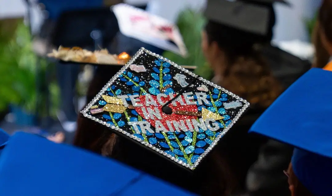 A COM Graduate's decorated cap reads 'Teacher in training'