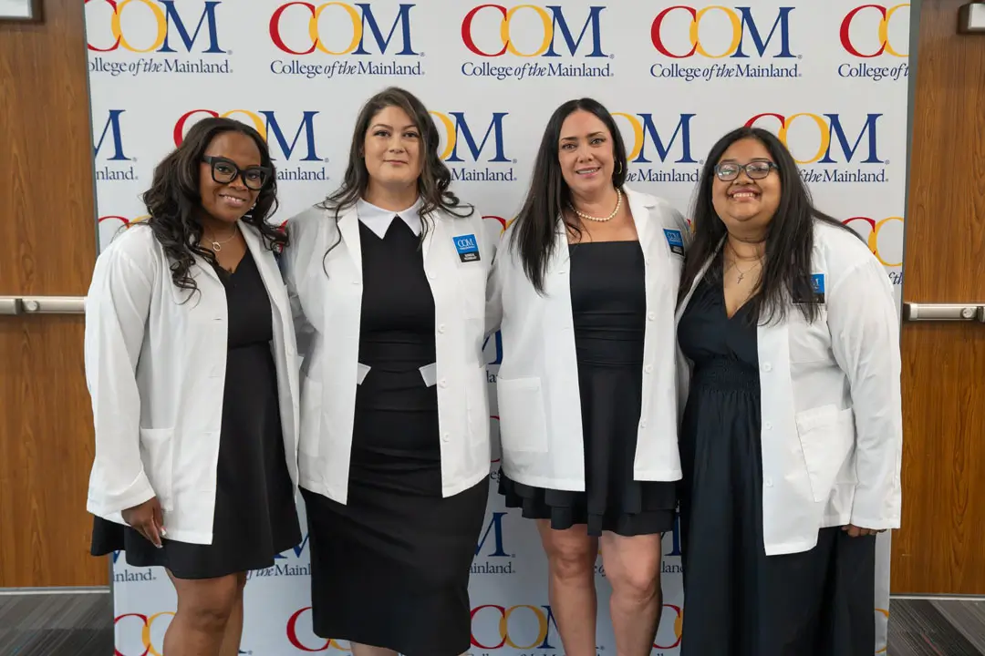 Photo of four graduates in front of COM backdrop