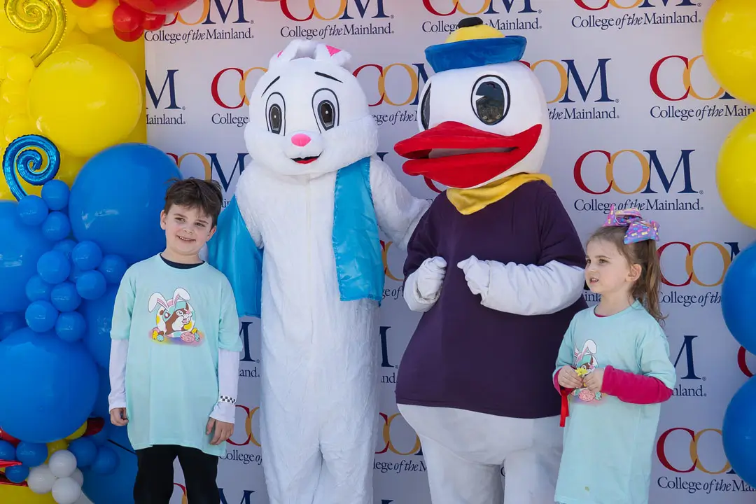 Two Flock the Block guests take a photo with the Easter Bunny and COM mascot.
