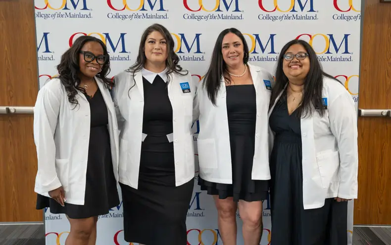 Photo of four graduates in front of COM backdrop