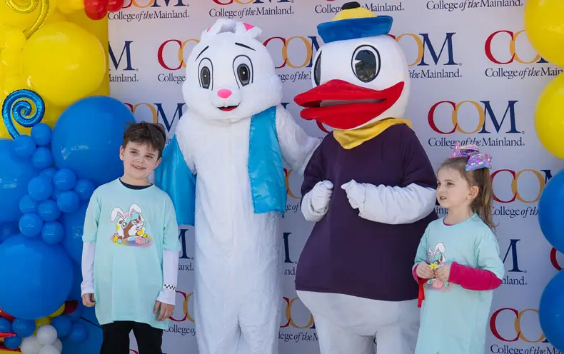Two Flock the Block guests take a photo with the Easter Bunny and COM mascot.