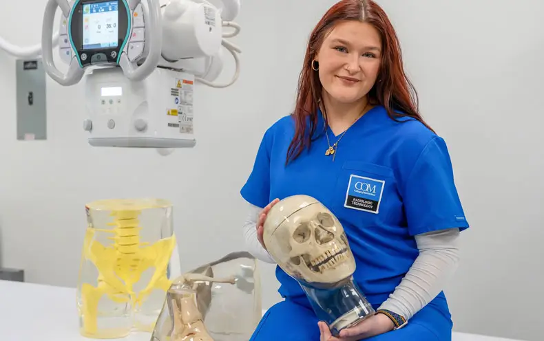 Amanda Respondek in the COM Rad Tech lab holding an x-ray skull model.