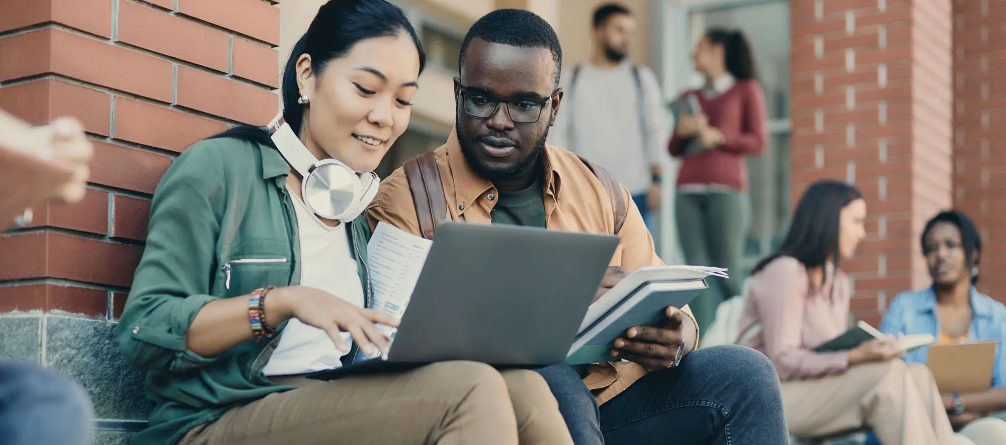 Young multiracial students use laptop while learning at campus.