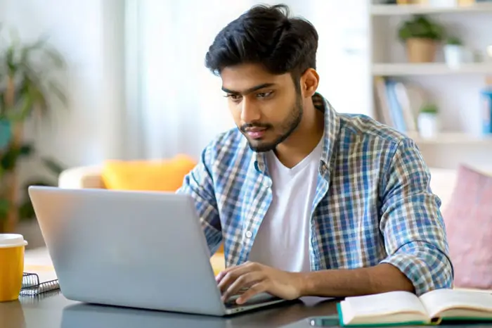 Young male student typing on laptop at home