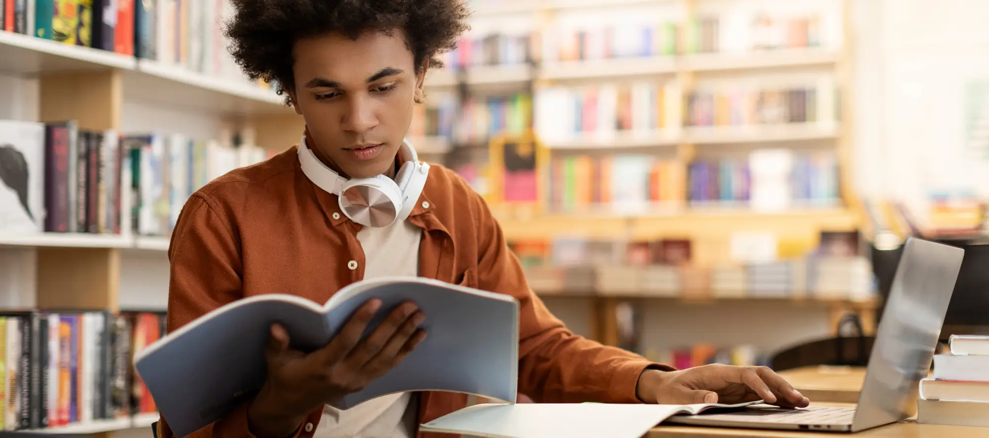 Student reading a book and working on laptop at school
