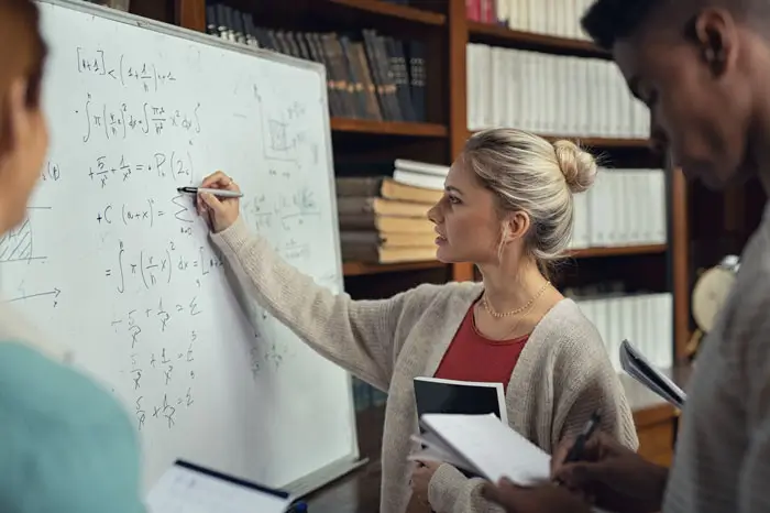 Female instructor at whiteboard giving a lecture to students standing nearby
