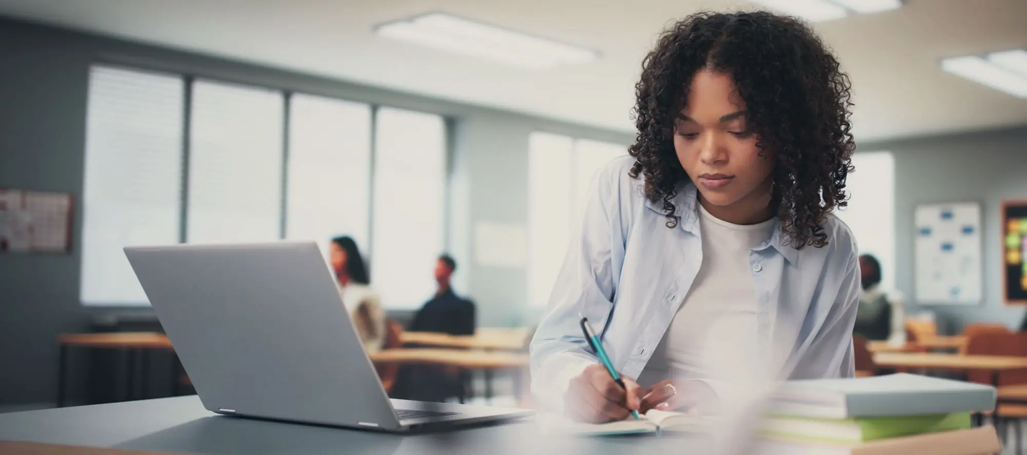 Young woman at a desk with laptop taking notes.