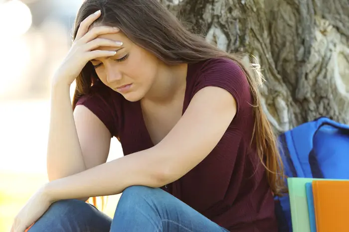 Sad girl leaning against a tree
