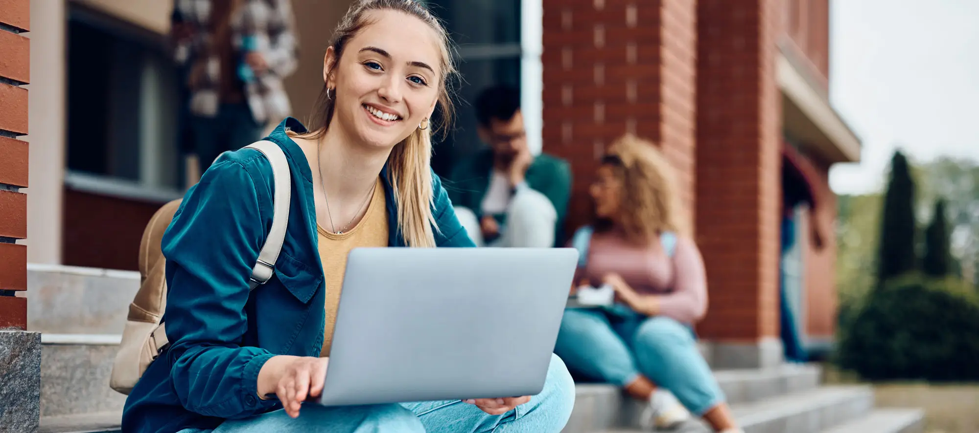 Female student with laptop sitting on building steps